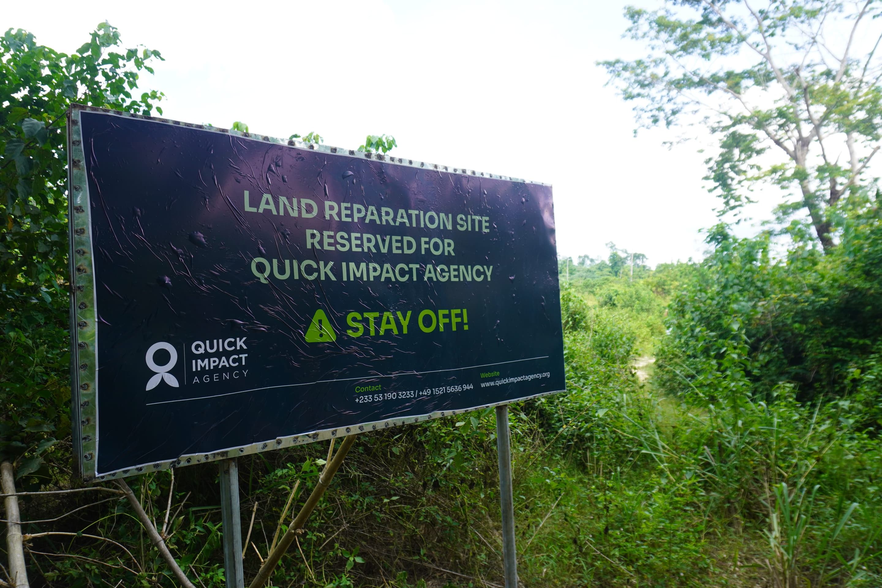 A QIA site notice reading Land Reparation Site Reserved For Quick Impact Agency, Stay Off, standing in regrowth on secured land